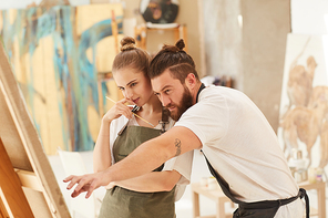 Warm-toned waist up portrait of contemporary couple painting picture together while standing by easel in art studio, copy space