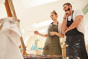 Warm-toned low angle view at creative couple painting picture together while standing by easel in art studio, copy space