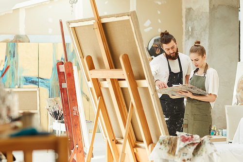 Wide angle portrait of creative couple painting picture together while standing by easel in art studio interior, copy space