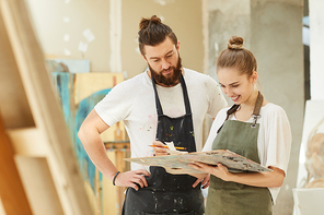 Waist up portrait of creative couple painting picture together while standing by easel in art studio interior, copy space