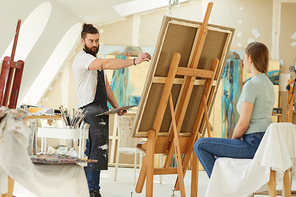 Portrait of male bearded artist painting portrait of young woman in studio, copy space