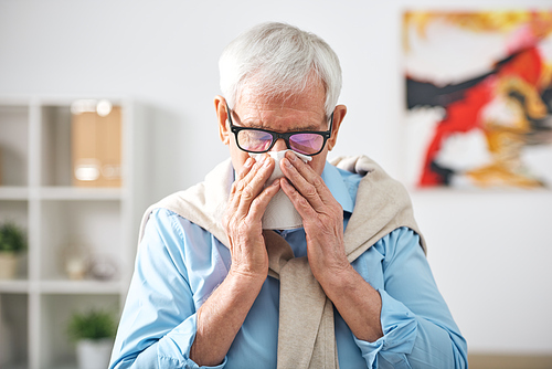 Sick senior retired man with handkerchief by his nose staying at home while feeling unwell during flu epidemy