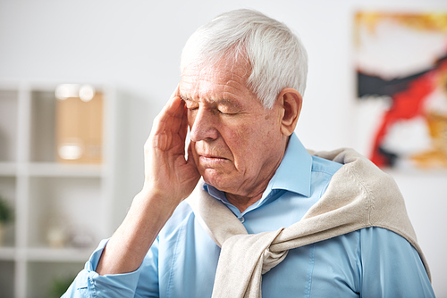 Exhausted senior white-haired man with closed eyes touching temple while feeling headache