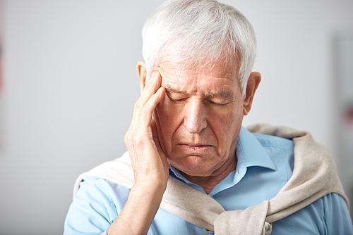 Sick senior man with whte hair and closed eyes touching head while having headache or expressing tiredness