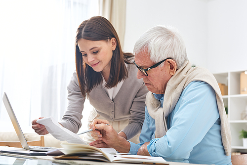 Content attractive young daughter assisting senior father to pay bills and check finances