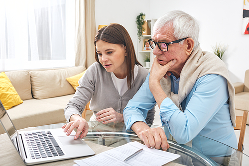 Senior man looking at laptop display while his daughter explaining him how to search information in the net