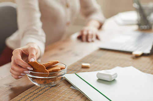 Warm-toned close up of unrecognizable woman taking homemade cookie while working at home, copy space