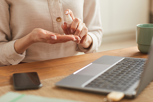Warm-toned close up of unrecognizable woman using hand sanitizer while working at home office, copy space