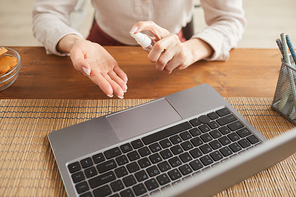 Warm-toned close up of unrecognizable woman spraying hand sanitizer while working at home office, copy space