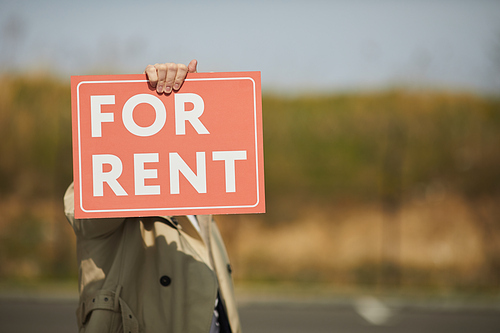 Background image of unrecognizable real estate agent holding red FOR RENT sign while standing in street outdoors, copy space