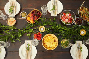 Top down view of colorful Summer dishes on wooden dinner table decorated with fresh leaves and floral elements during outdoor party, copy space