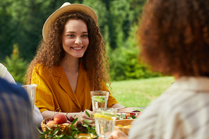 Colorful portrait of smiling young woman enjoying dinner with friends outdoors while sitting at table during Summer party, copy space