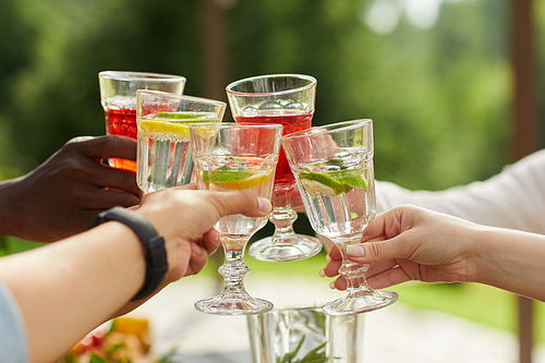 Close up of multi-ethnic group of friends clinking cocktail glasses while enjoying outdoor party in Summer, copy space