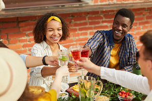 Multi-ethnic group of friends toasting while enjoying outdoor dinner in Summer, focus on young African-American woman smiling cheerfully, copy space