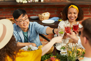 Multi-ethnic group of friends toasting while enjoying outdoor dinner in Summer, focus on young Asian man smiling cheerfully, copy space