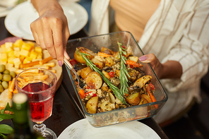 Close up of unrecognizable woman holding dish with golden roasted potatoes while enjoying dinner with friends and family outdoors, copy space