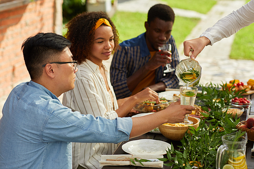 Multi-ethnic group of young people pouring drinks while enjoying dinner with friends and family outdoors at Summer party, copy space
