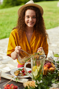Vertical portrait of smiling young woman  while enjoying dinner with friends and family outdoors at Summer party