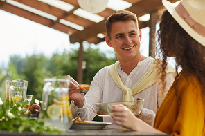 Portrait of smiling young man looking at girlfriend while enjoying dinner with friends and family outdoors at Summer party, copy space