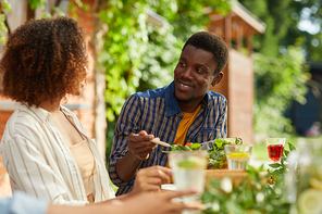 Portrait of smiling African-American man looking at girlfriend while enjoying dinner with friends and family outdoors at Summer party, copy space