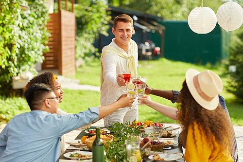 Portrait of smiling young man toasting with friends while enjoying dinner at outdoor terrace in Summer, copy space