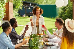 Portrait of young African-American woman laughing cheerfully while enjoying dinner with friends at outdoor terrace in Summer, copy space