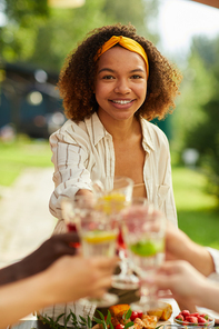 Vertical portrait of smiling young woman toasting with friends while enjoying dinner at outdoor terrace in Summer