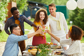 Multi-ethnic group of friends clinking glasses while enjoying dinner outdoors at Summer party, copy space