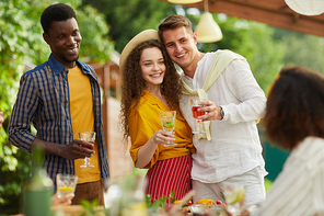 Portrait of young couple embracing while standing by table and enjoying dinner with friends outdoors at Summer party, copy space