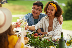 Portrait of mixed-race young couple toasting while enjoying dinner with friends outdoors at Summer party, copy space