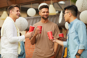 Waist up portrait of young men drinking beer and hatting during outdoor party in Summer, copy space