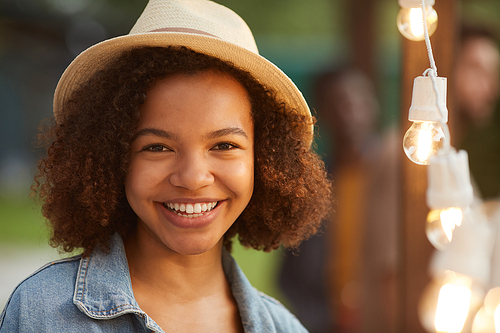 Candid close up portrait of smiling African-American woman  while standing by lights at outdoor party