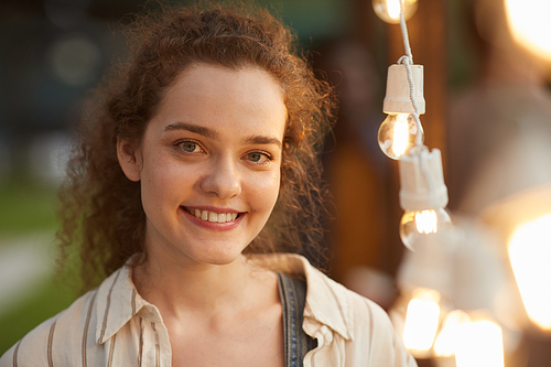 Candid close up portrait of smiling young woman  while standing by lights at outdoor party