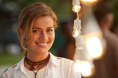 Candid close up portrait of smiling woman  while standing by lights at outdoor party