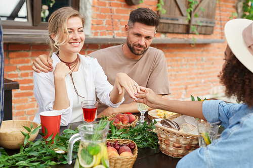 Portrait of beautiful blonde woman showing off engagement ring to friends during outdoor dinner, copy space