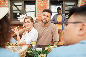Multi-ethnic group of people enjoying dinner outdoors, focus on couple speaking to friends, copy space