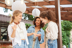 Waist up portrait of smiling young woman showing engagement ring to girlfriends during outdoor party, copy space