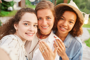 POV portrait of beautiful young woman showing engagement ring taking selfie with friends during outdoor party