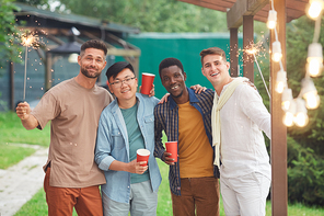 Multi-ethnic group of male friends  and holding sparklers while enjoying party outdoors, copy space