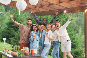 Multi-ethnic group of happy friends holding sparklers and  while enjoying Summer party outdoors, copy space