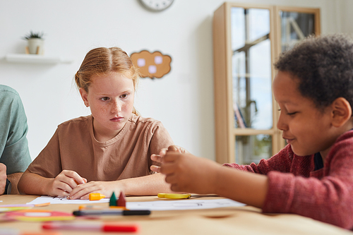 Portrait of freckled red haired girl looking at friend while drawing pictures together during art class in school, copy space