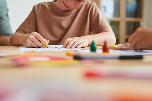 Close up of freckled girl drawing pictures with crayons while enjoying art class in preschool, copy space