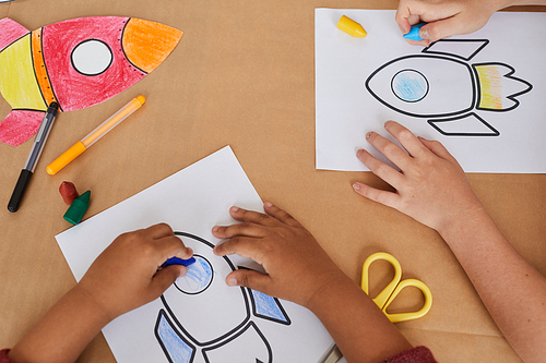 Top view close up of unrecognizable little kids drawing pictures of space rockets while enjoying art class in preschool or development center, copy space