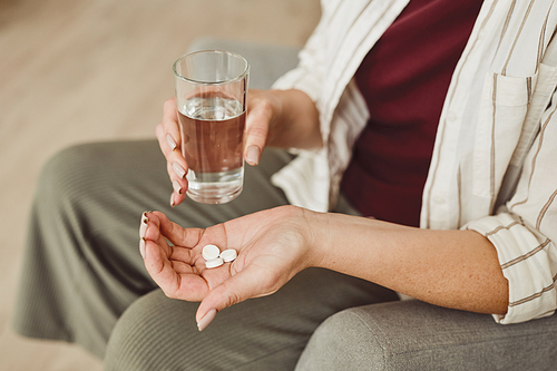 Warm toned close up of unrecognizable woman holding pills and glass of water, medicine and recovery treatment, copy space