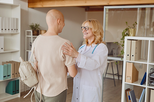 Warm-toned portrait of cheerful female doctor greeting bald patient and congratulating her on cancer recovery, copy space