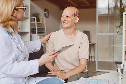 Warm toned portrait of smiling bald woman talking to female doctor during consultation on alopecia and cancer recovery, copy space