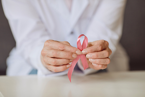 Close up background image of unrecognizable female doctor holding pink ribbon against white lab coat as symbol of breast cancer awareness, copy space