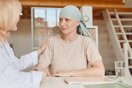 Warm-toned portrait of mature bald woman talking to female doctor comforting and congratulating her during consultation on alopecia and cancer recovery, copy space