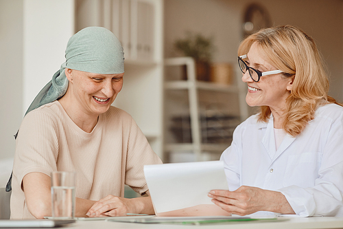 Warm-toned portrait of smiling bald woman listening to female doctor showing negative test results during consultation on alopecia and cancer recovery, copy space