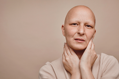 Minimal head and shoulders portrait of bald woman looking at camera while posing against beige background in studio, alopecia and cancer awareness, copy space